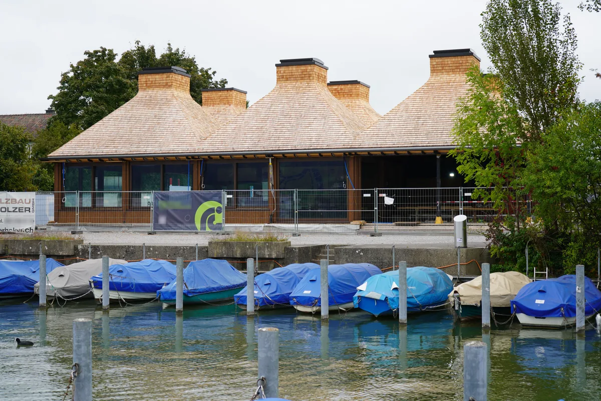 Neubau am Greifensee: Im Seerestaurant im Schilf will die Gastro Buddies AG spätestens im Dezember Gäste bewirten.  Letzte Bauphase vom Seerestaurant in Niederuster. Ein Holzbau mit auffälligem Dach, das aus sechs Giebeln besteht. Davor schaukeln Boote, die mit blauen Blachen abgedeckt sind.